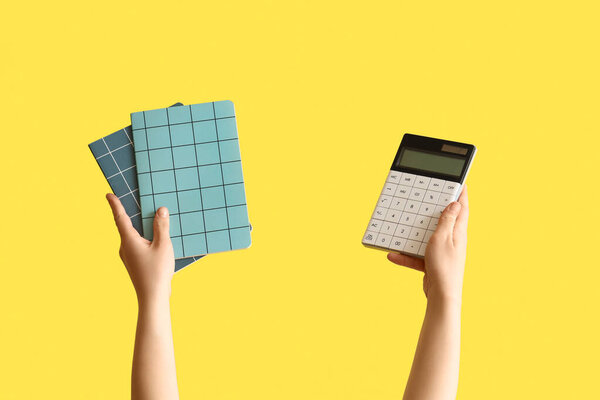 Female hands holding notebooks and calculator on yellow background