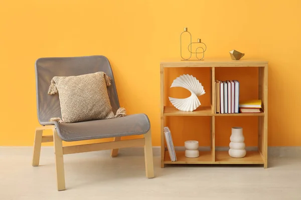 Shelving unit with books, decor and chair near orange wall in room