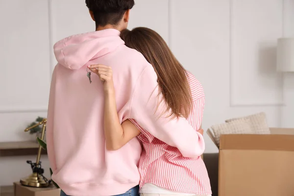 Young couple with keys hugging in their new flat, back view