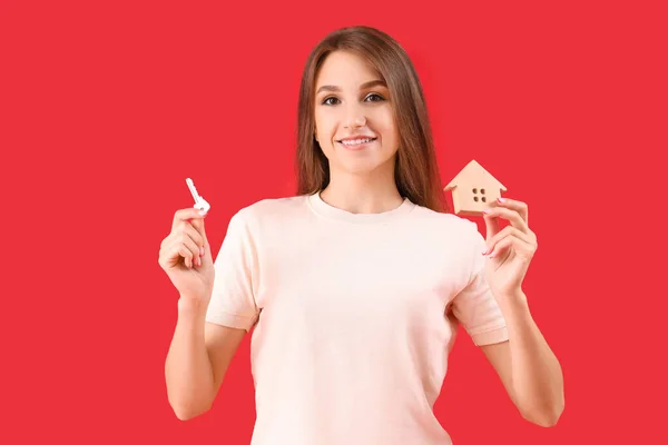 Junge Frau Mit Schlüssel Und Hausfigur Auf Rotem Hintergrund — Stockfoto