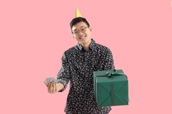Young Asian man with money and birthday gift on pink background