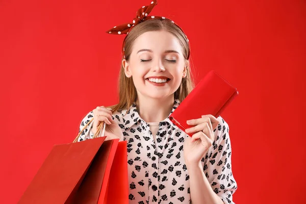 ショッピングバッグと赤い背景の財布を持つ幸せな若い女性 — ストック写真