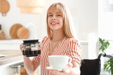 Tekerlekli sandalyedeki genç kadın evde kahve içiyor.