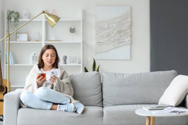 Evde boş gününde cep telefonu kullanan çay içen genç bir kadın.