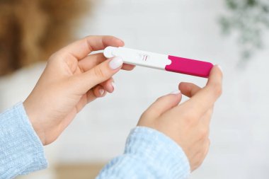 Bulanık arka planda pozitif hamilelik testi olan kadın eller, yakın plan.