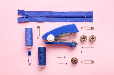 Pembe arka planda farklı malzemelerle elle dikiş makinesi.