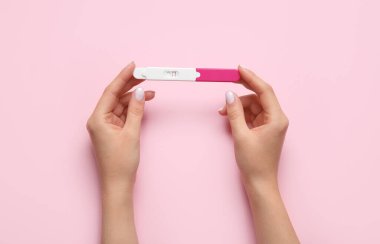 Pembe arka planda hamilelik testi olan kadın eller.