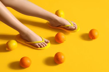 Şık parmak arası terliklerle sarı arka planda turunçgillerle kadın bacakları.