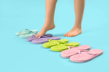 Mavi arka planda farklı renkte parmak arası terlikleri olan kadın bacakları.