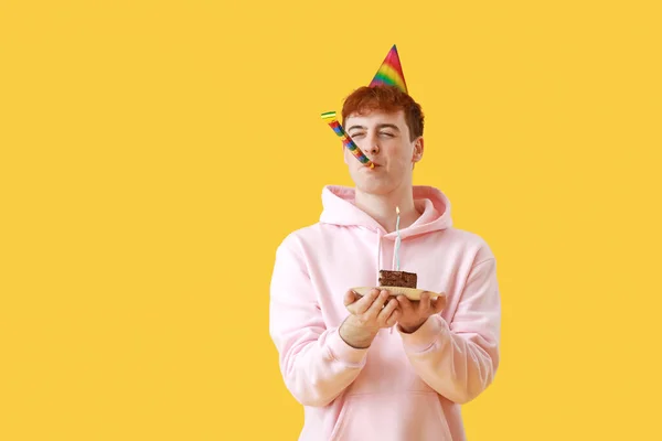 Young man with party blower and piece of birthday cake on yellow background
