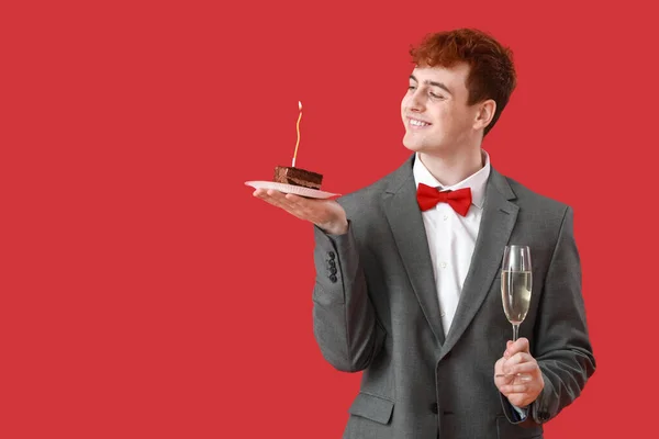 Young man with piece of birthday cake and champagne on red background