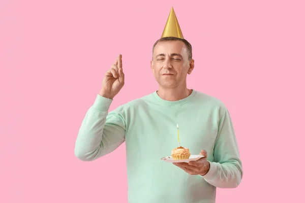 Mature man with birthday tartlet making wish on pink background