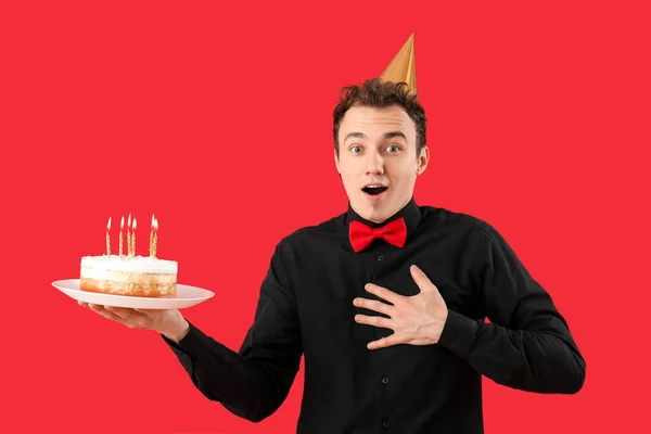 Surprised young man with birthday cake on red background