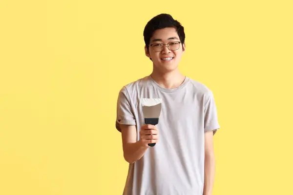 黄色の背景にパティナイフを持つ若いアジアの男 — ストック写真