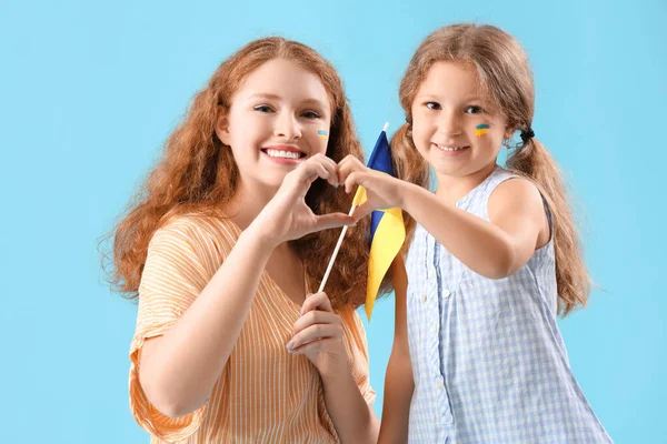 幸せな少女とウクライナの旗を持つ彼女の母親は 青い背景に心のジェスチャーを示しています — ストック写真