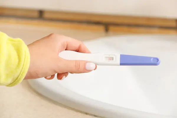 Woman with pregnancy test near sink, closeup