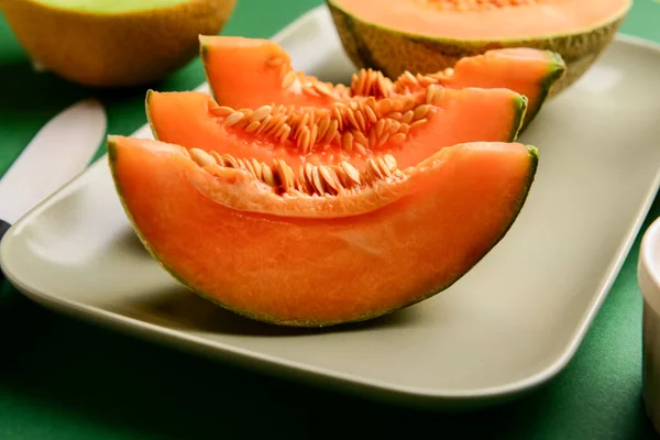 Plate with slices of ripe melon on green background