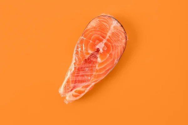 Fresh salmon steak in plastic food wrap on orange background