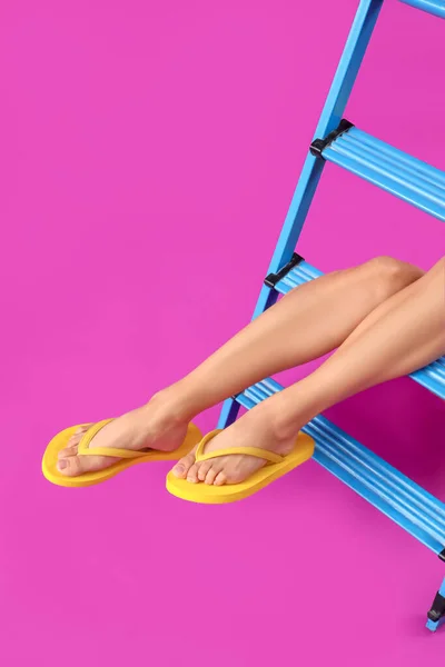 Legs of young woman in flip-flops on magenta background