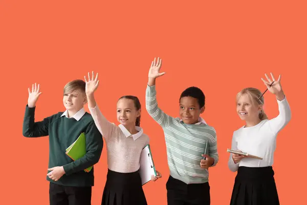 Kis Osztálytársak Elegáns Egyenruhában Jegyzetfüzetekkel Kezekkel Narancssárga Háttéren — Stock Fotó