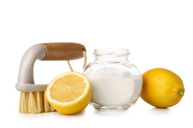 Beyaz arka planda bir kavanoz kabartma tozu, limon ve temizlik fırçası.