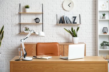 Workplace with laptop, stylish holder for books and lamp in room clipart