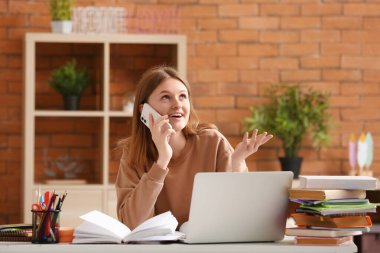 Evde ders yaparken cep telefonuyla konuşan genç bir kız.