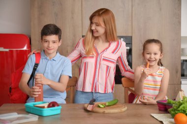 Anne, küçük çocuklarına mutfakta öğle yemeği hazırlıyor.