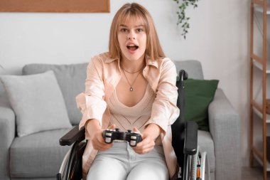 Tekerlekli sandalyedeki genç kadın evde video oyunu oynuyor.