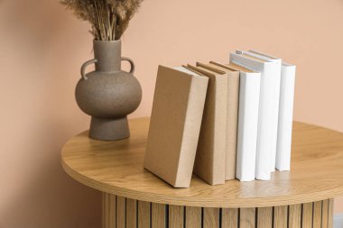 Bej duvarın yanındaki masada otlu vazo ve kitaplar.