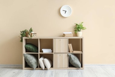 Odadaki bej duvarın yanında içinde kitap, yastık ve çiçek bulunan çekmeceler.