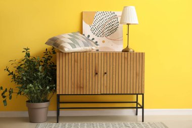 Ahşap dolap, masa lambası, yastık ve sarı duvarın yanında boya.