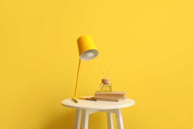 Sarı duvarın yanında lamba, kitap ve kamış ayırıcılı küçük masa