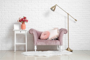 Beyaz tuğla duvarın yanındaki sehpanın üzerinde şakayık çiçekleri olan rahat bir koltuk ve vazo.