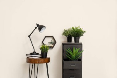 Masa lambası küçük masada ve dosya dolabında beyaz duvarın yanında bitkiler var
