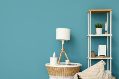 Lamba küçük masada ve raf ünitesi mavi duvarın yanında.