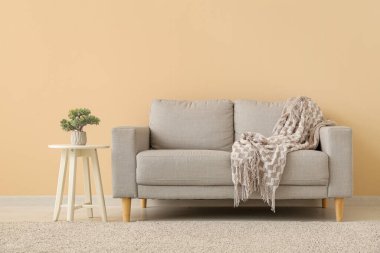 Gri kanepe ve dekoratif ağaç bej duvarın yanındaki küçük masada.