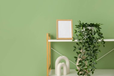 Boş çerçeveli raf ünitesi, yeşil duvarın yanında ev bitkisi ve dekor.