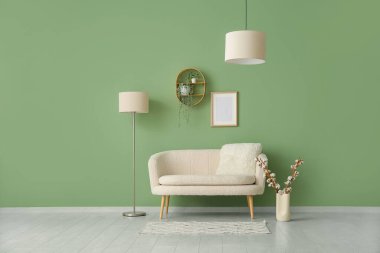 Yeşil duvarın yanındaki vazoda yastıklı ve pamuklu kanepe.