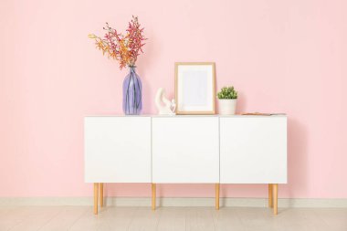 Boş çerçeveli beyaz büfe, çiçekler ve pembe duvarın yanındaki çiçek.