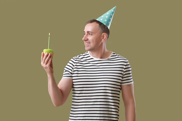 Mature man with birthday tartlet on green background