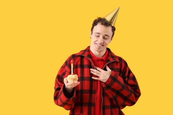 Young man with birthday cake on yellow background