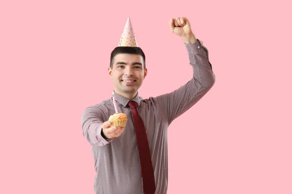 Happy young man with birthday cake on pink background