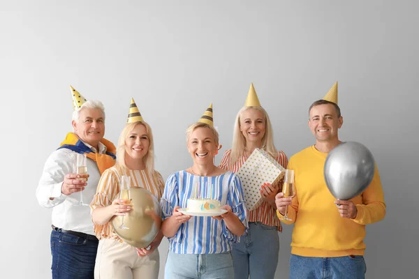 Mature people with cake and champagne celebrating Birthday on light background