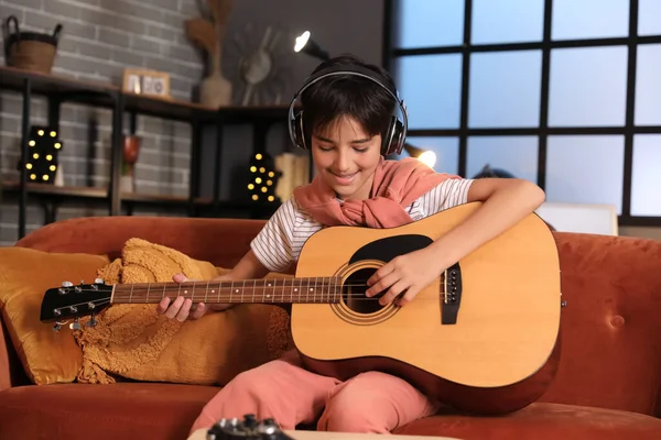 Little boy with headphones playing guitar at home late in evening