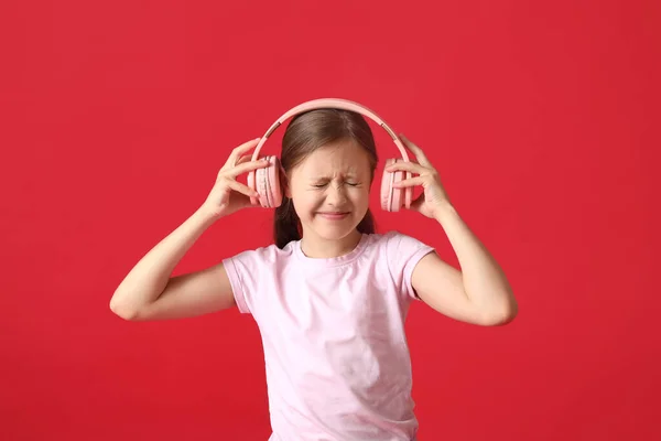 Kırmızı Arka Planda Kulaklıkları Olan Hoşnutsuz Küçük Bir Kız — Stok fotoğraf