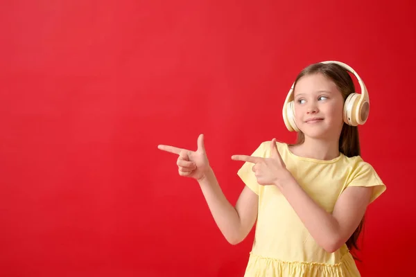 Little girl in headphones pointing at something on red background