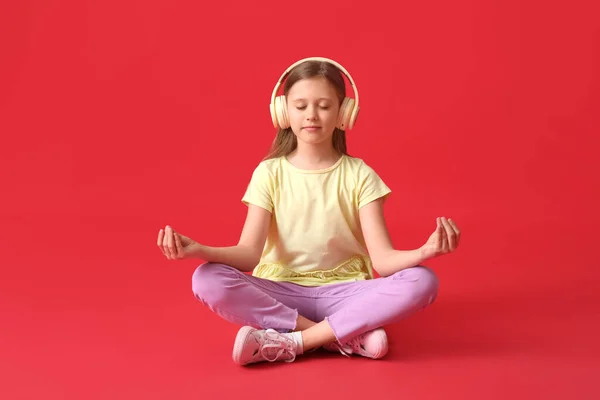 小さな女の子でヘッドフォン瞑想で赤の背景 — ストック写真