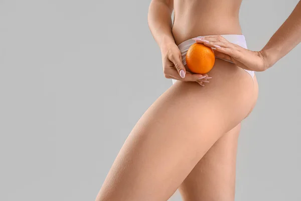 Young woman with cellulite problem and orange on light background, closeup
