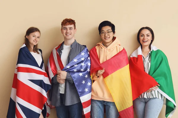 Young students of language school with flags on beige background